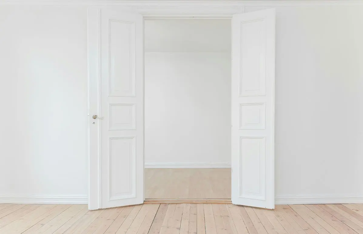 A white room with two doors open and the floor is bare.